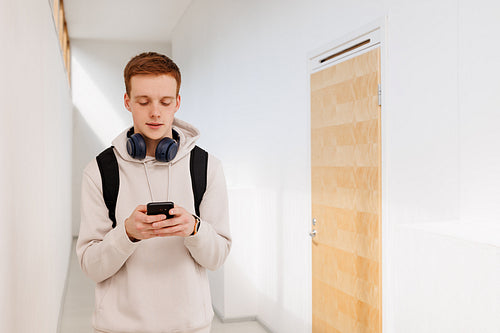 Male student walking in the corridor and using a smartphone