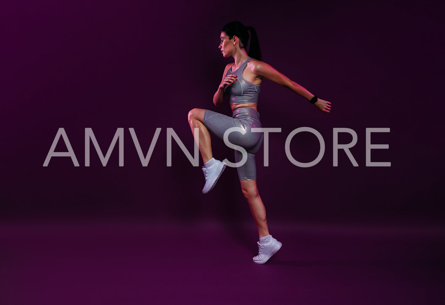 Full length of a young slim jogger practicing over a magenta backdrop. Female in silver fitness attire jumping.