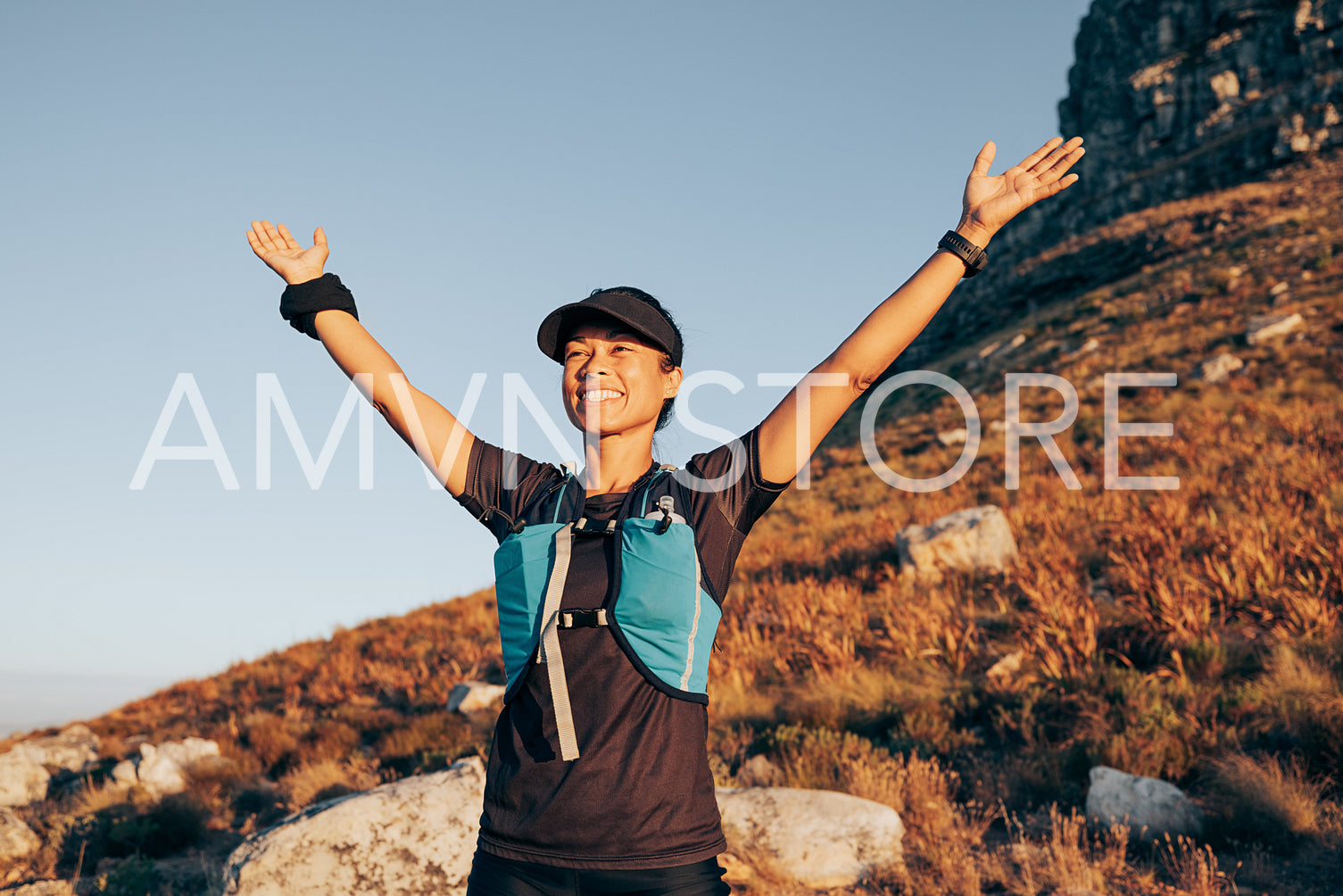 Happy woman enjoying sunset during hike. Smiling female standing on hill with raised arms.