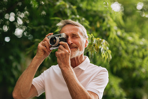 Senior man making photographs on film camera while walking outdoors