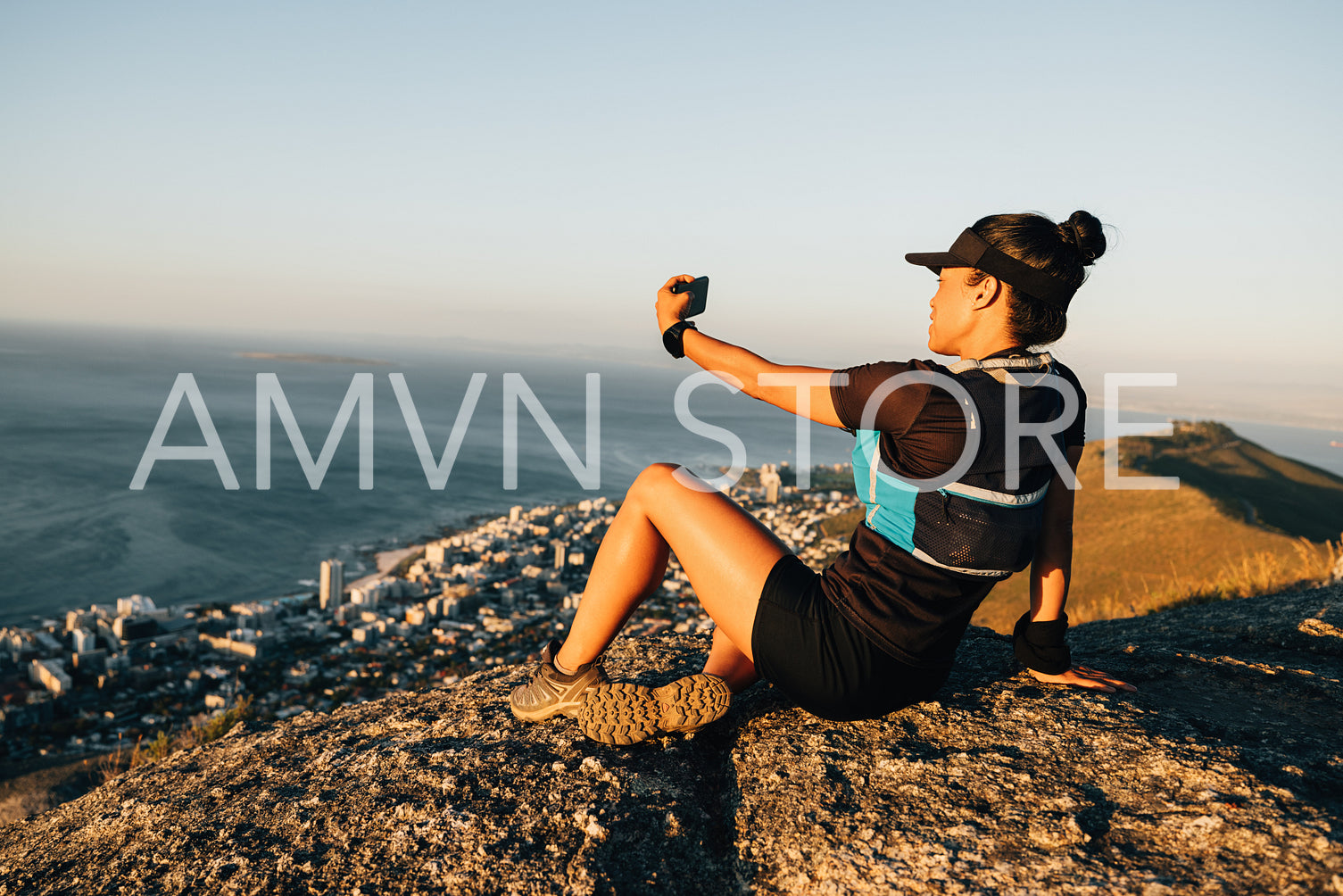 Young woman in sportswear relaxing after hike and making selfie while sitting on rock