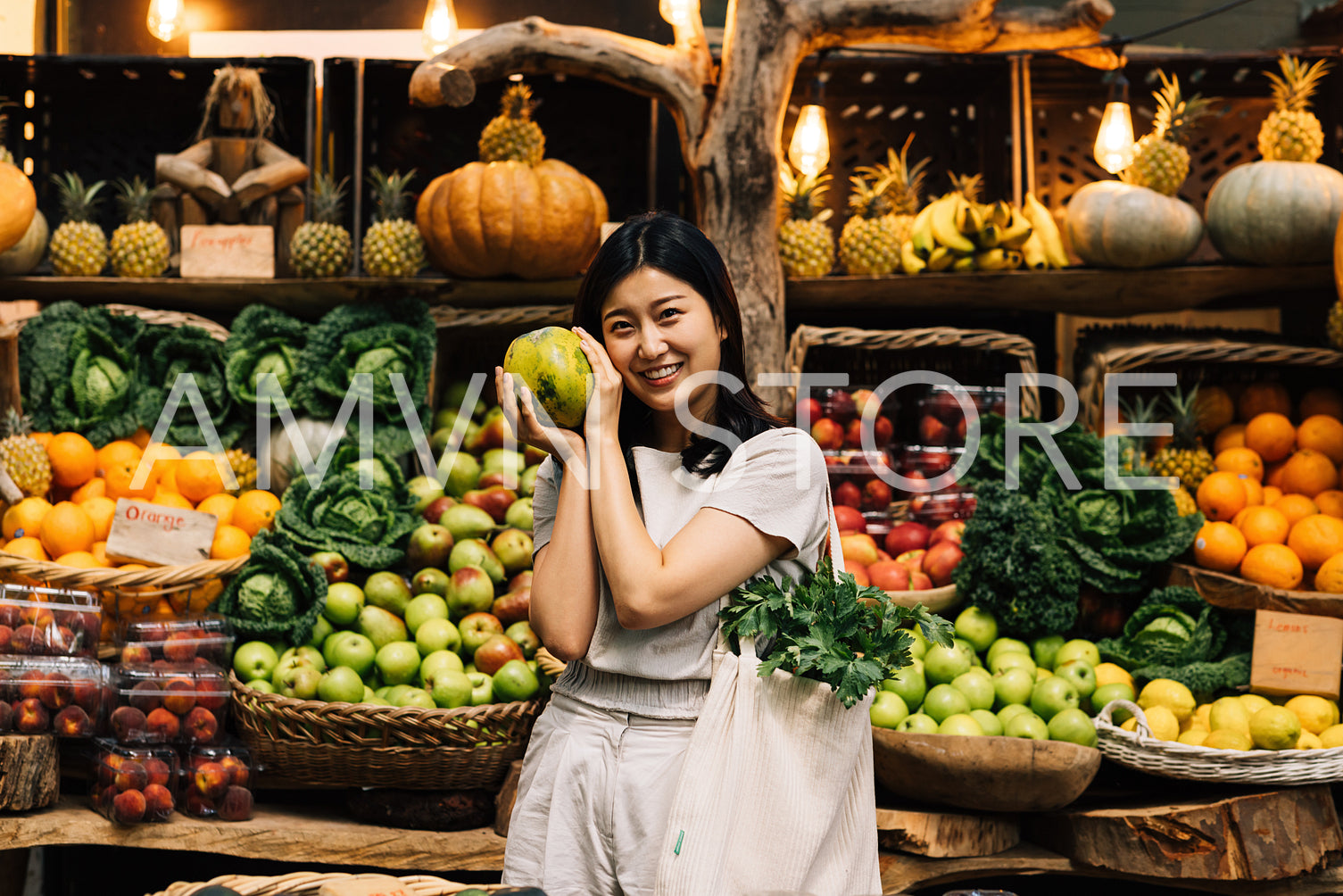 Cheerful woman holding fruit and looking at a camera while standing on a local outdoor market