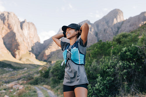 Laughing woman in sportswear relaxing during hike. Smiling female in wild terrain looking away.