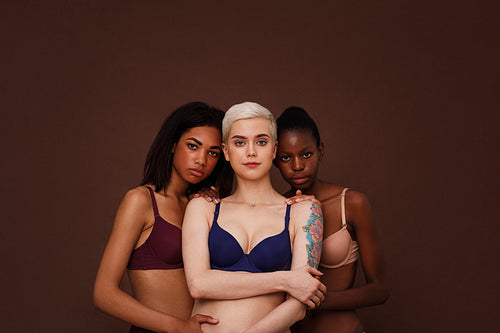 Three women of different skin color standing together. Group of young female in lingerie against backdrop.