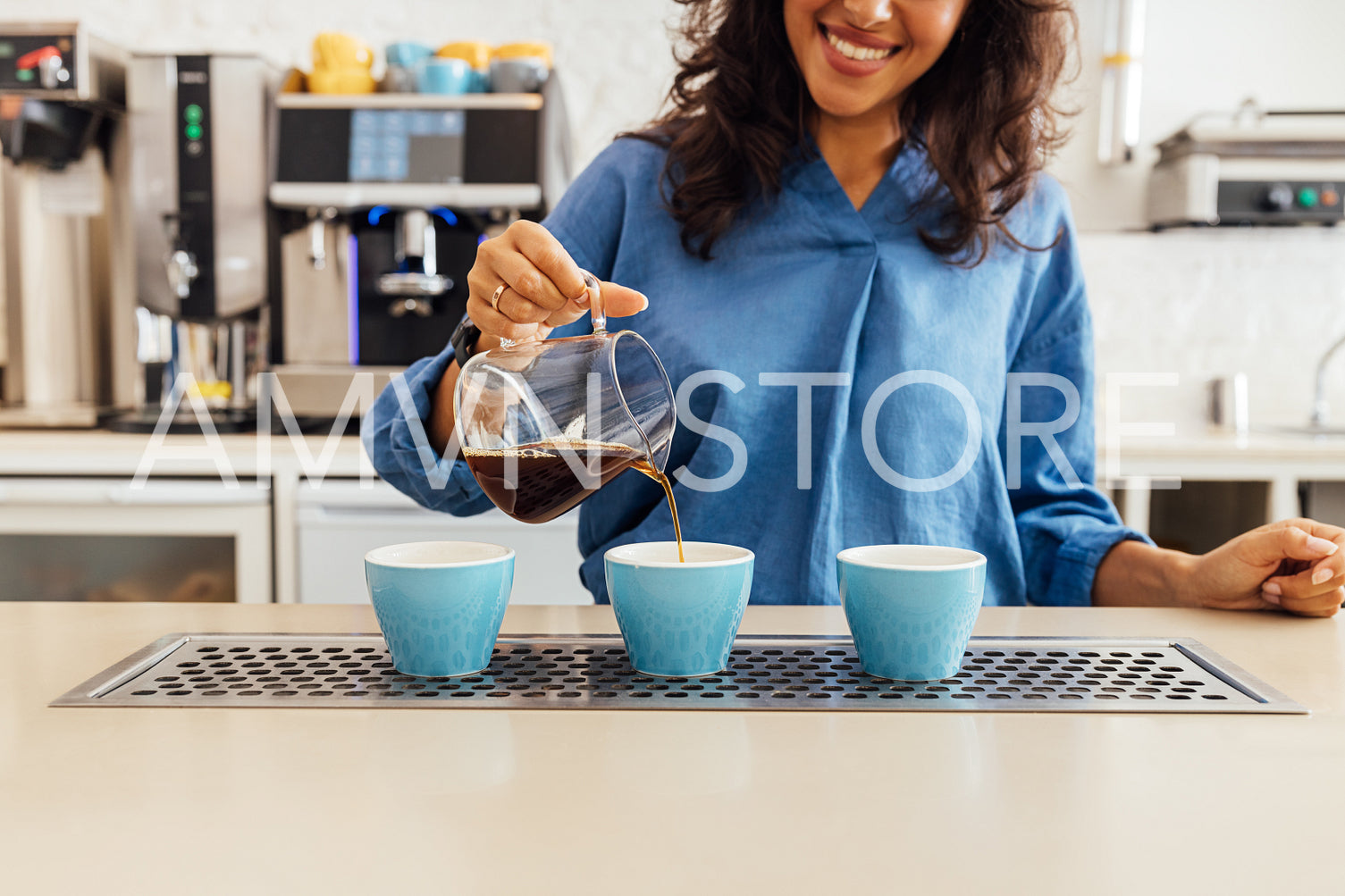 Unrecognizable smiling barista pouring coffee from glass teapot in three blue cups	