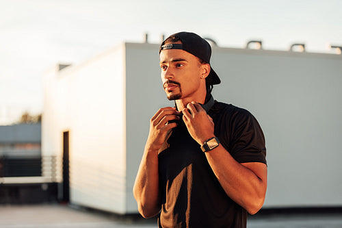 Confident male athlete standing on the roof at sunset and looking away