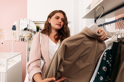 Young woman holding a hanger in small boutique choosing clothes