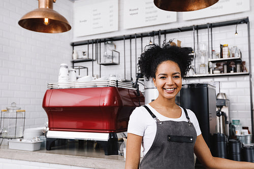 Young happy barista standing in cafe wearing apron