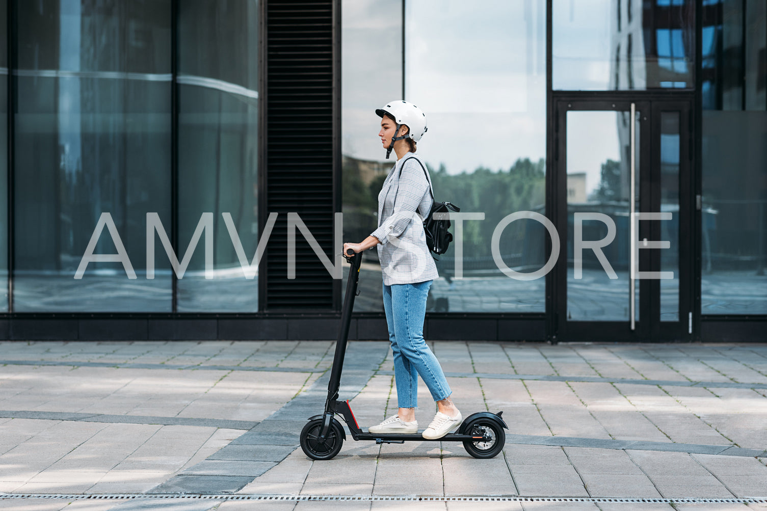 Side view of a young businesswoman riding electric push scooter. Female in cycling helmet driving electrical scooter against building.