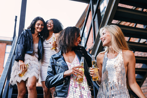 Happy women walking with bottles of beers. Young female friends having fun while stepping down stairs.