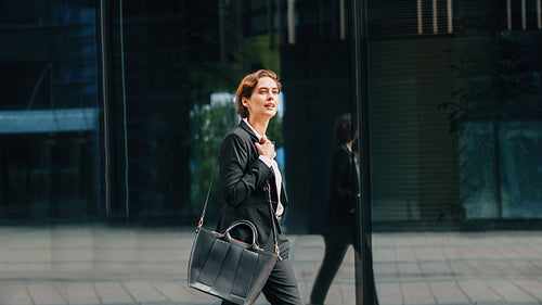 Side view of young businesswoman carrying a bag walking in front of an office building