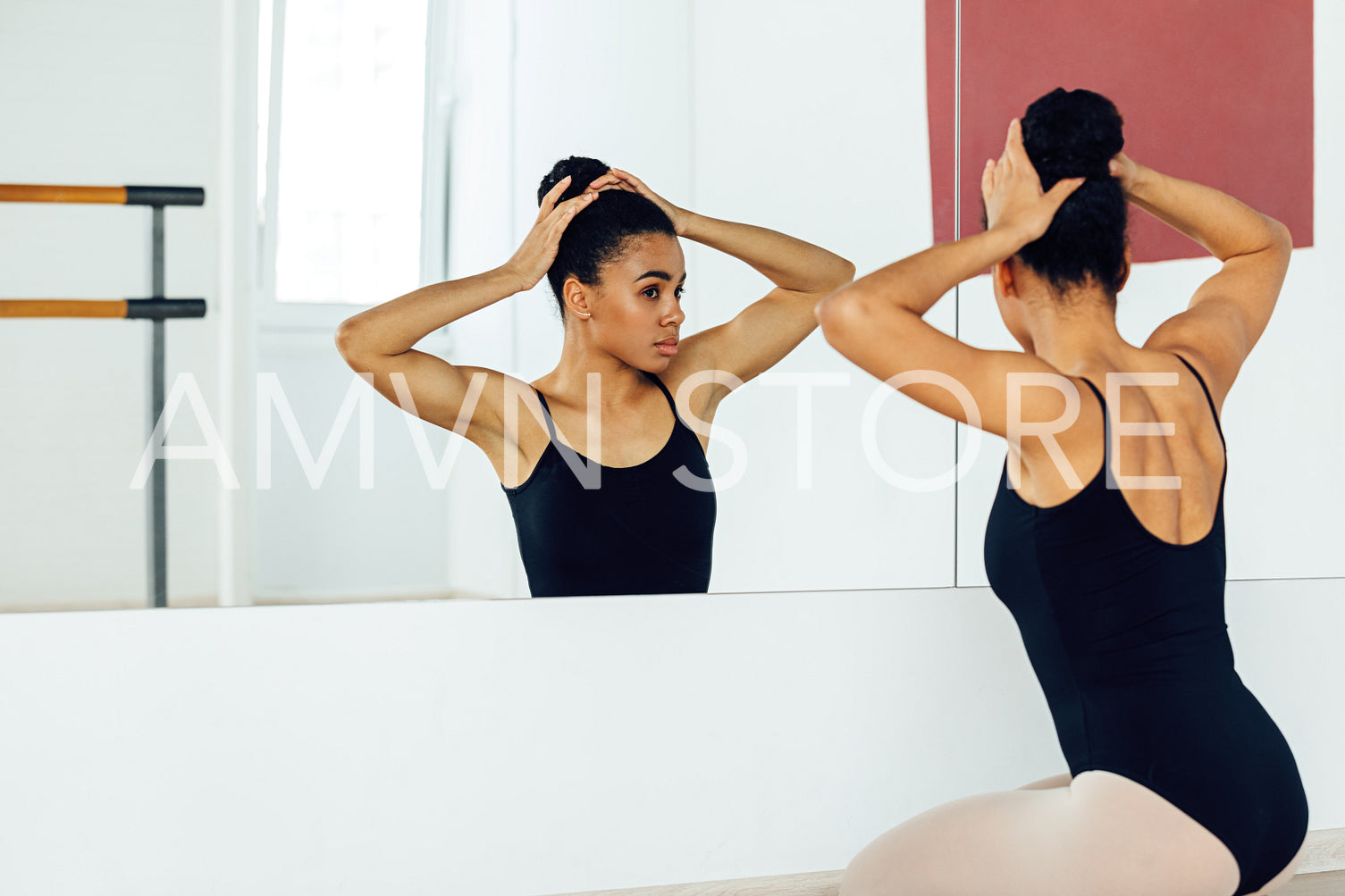 Rear view of young ballerina sitting in front of a mirror and adjusting her hair	