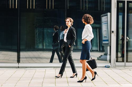 Two women commuting to the office in the day carrying office bags. Ceo and her assistant walking on a city street.