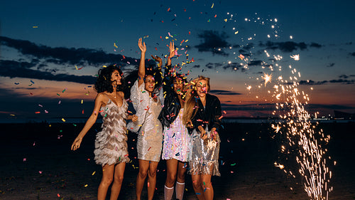 Four women celebrating at sunset. Happy female friends dancing between fireworks at dusk.