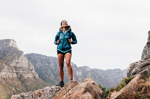 Woman in sports clothes with backpack standing on a rock and looking up during mountain hike