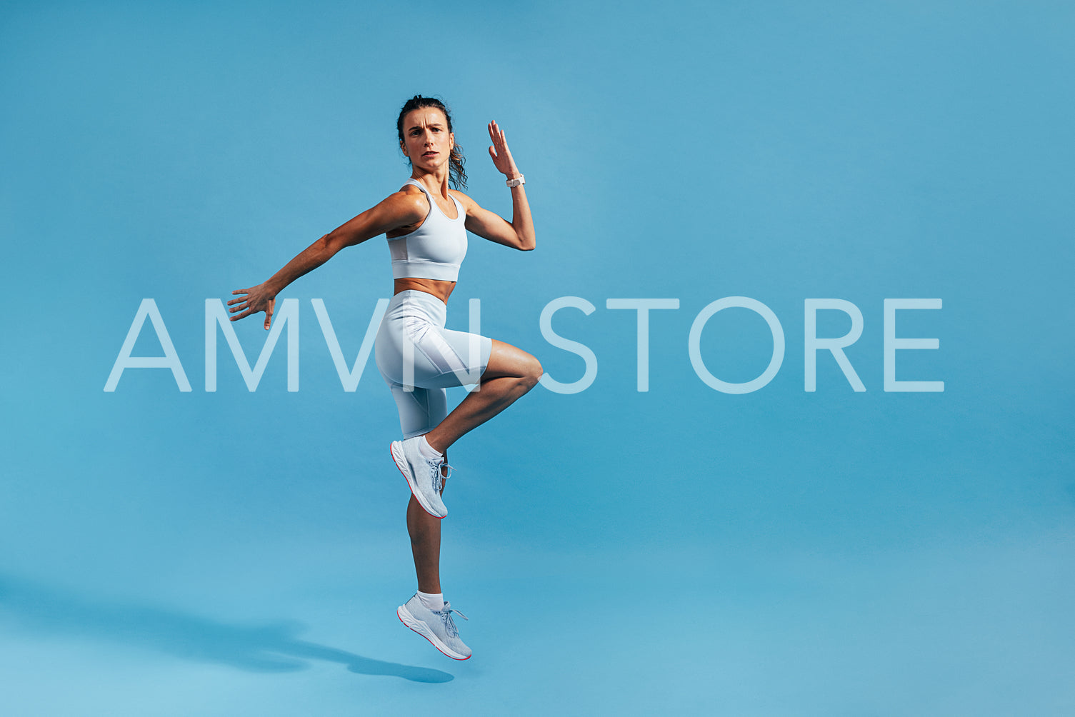 Slim woman jumping in studio on blue background. Muscular female in fitness clothes exercising.