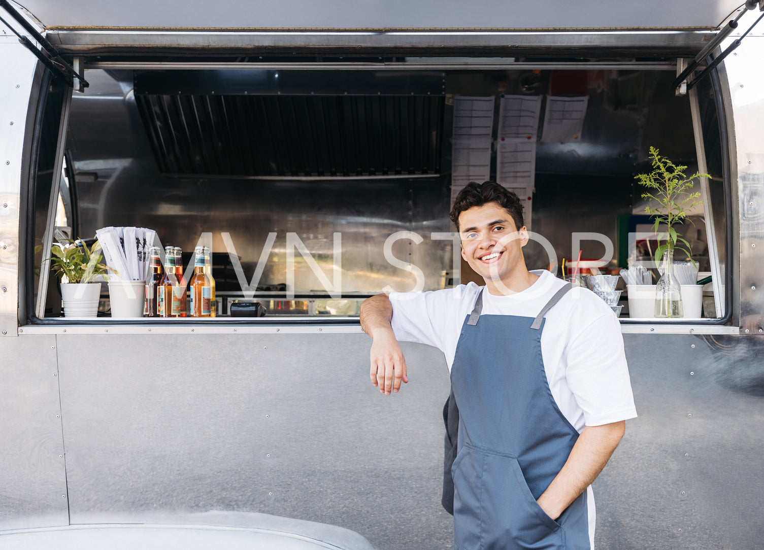 Handsome waiter leaning on a food truck. Young business owner waiting for customers.