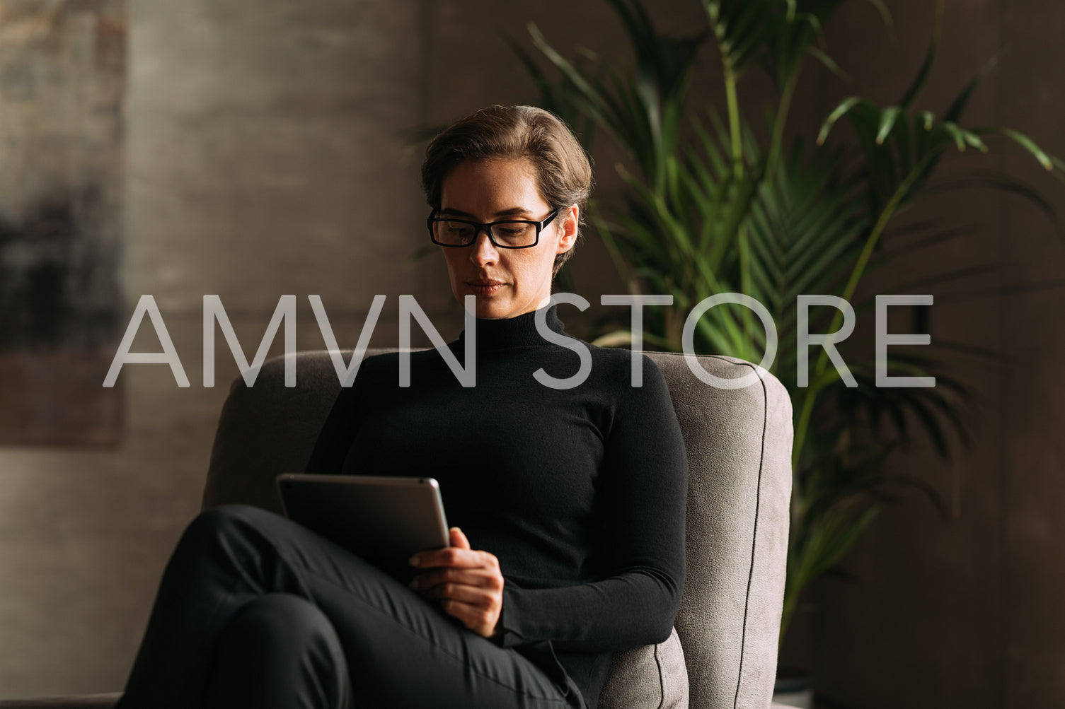 Serious adult woman in black formal wear sitting and reading from a digital tablet