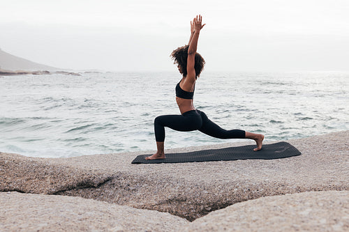 Fit woman stretching on the beach at sunset. Side view of young female practicing yoga.