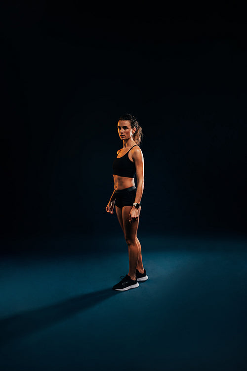 Portrait of young woman in sportswear relaxing on black background during training