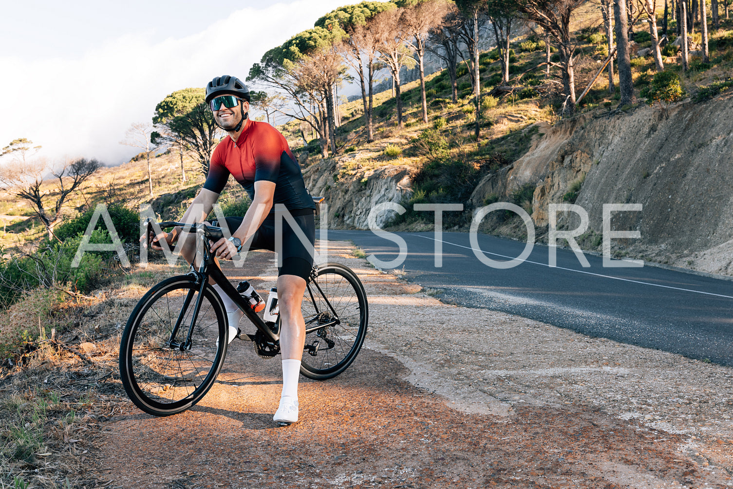 Smiling cyclist standing on a roadside in wild terrain. Male bike rider standing with his bicycle at taking a break.