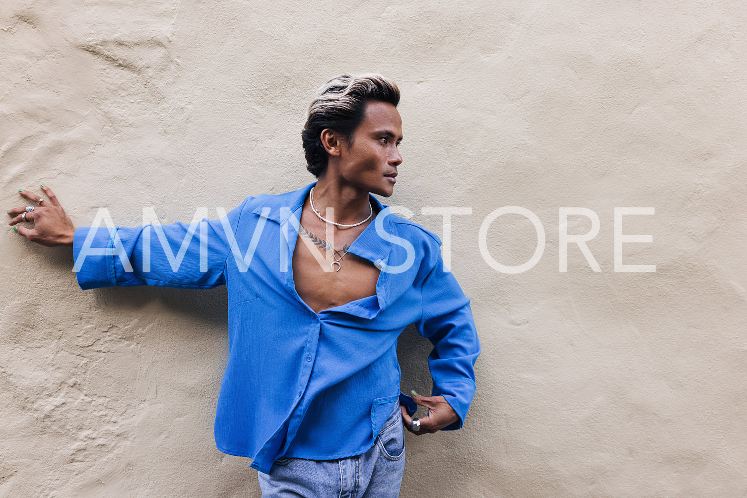 Side view of a young guy in a blue shirt leaning on a wall and looking away