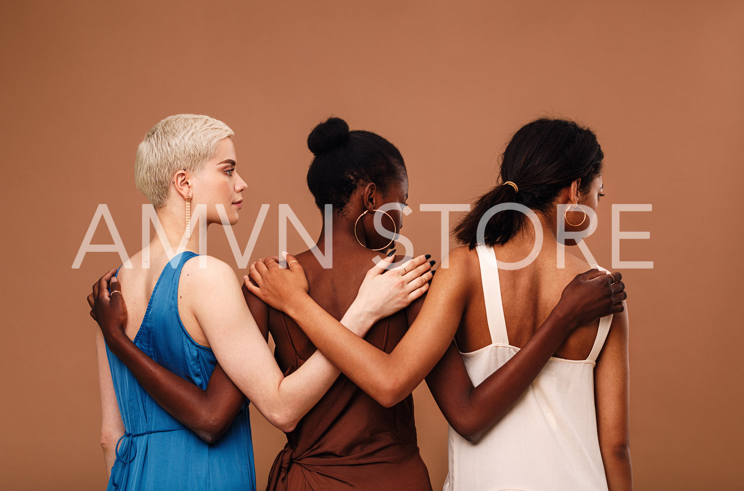 Three diverse women standing against brown background hugging each other	