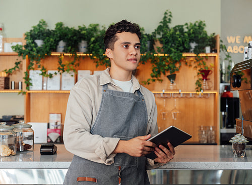 Male bartender holding a digital tablet at counter. Coffee shop owner with a portable computer.