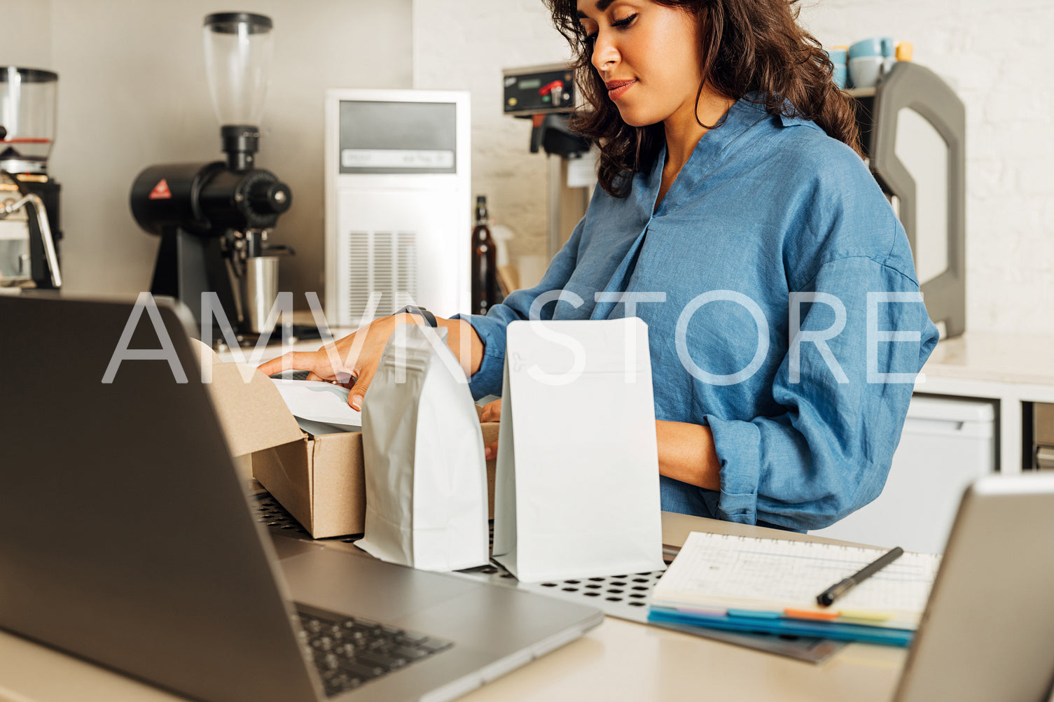 Woman working in her small cafe puts packs of coffee in a delivery box. Business owner preparing parcel.