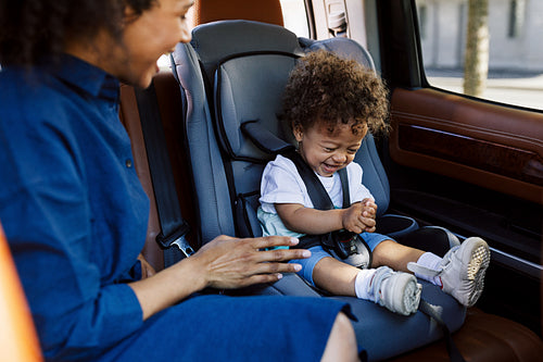 Young mother and her little son laughing together while sitting on the backseat of a car