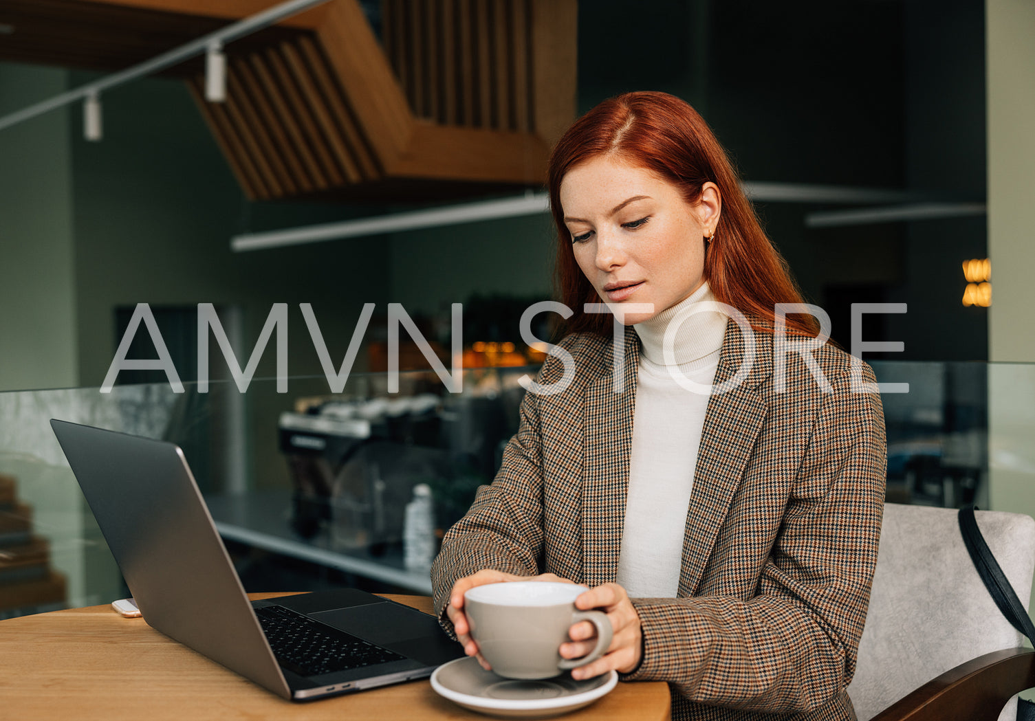 Young female entrepreneur in a cafe in morning. Woman with ginger hair working from a coffee shop.