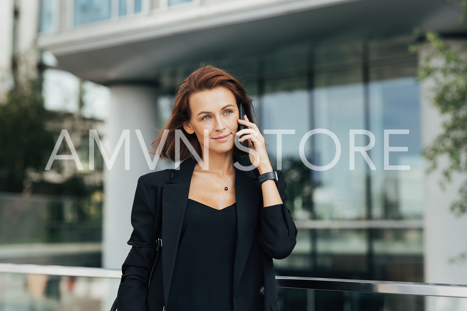 Confident businesswoman with ginger hair making a phone call while walking outdoors against office building