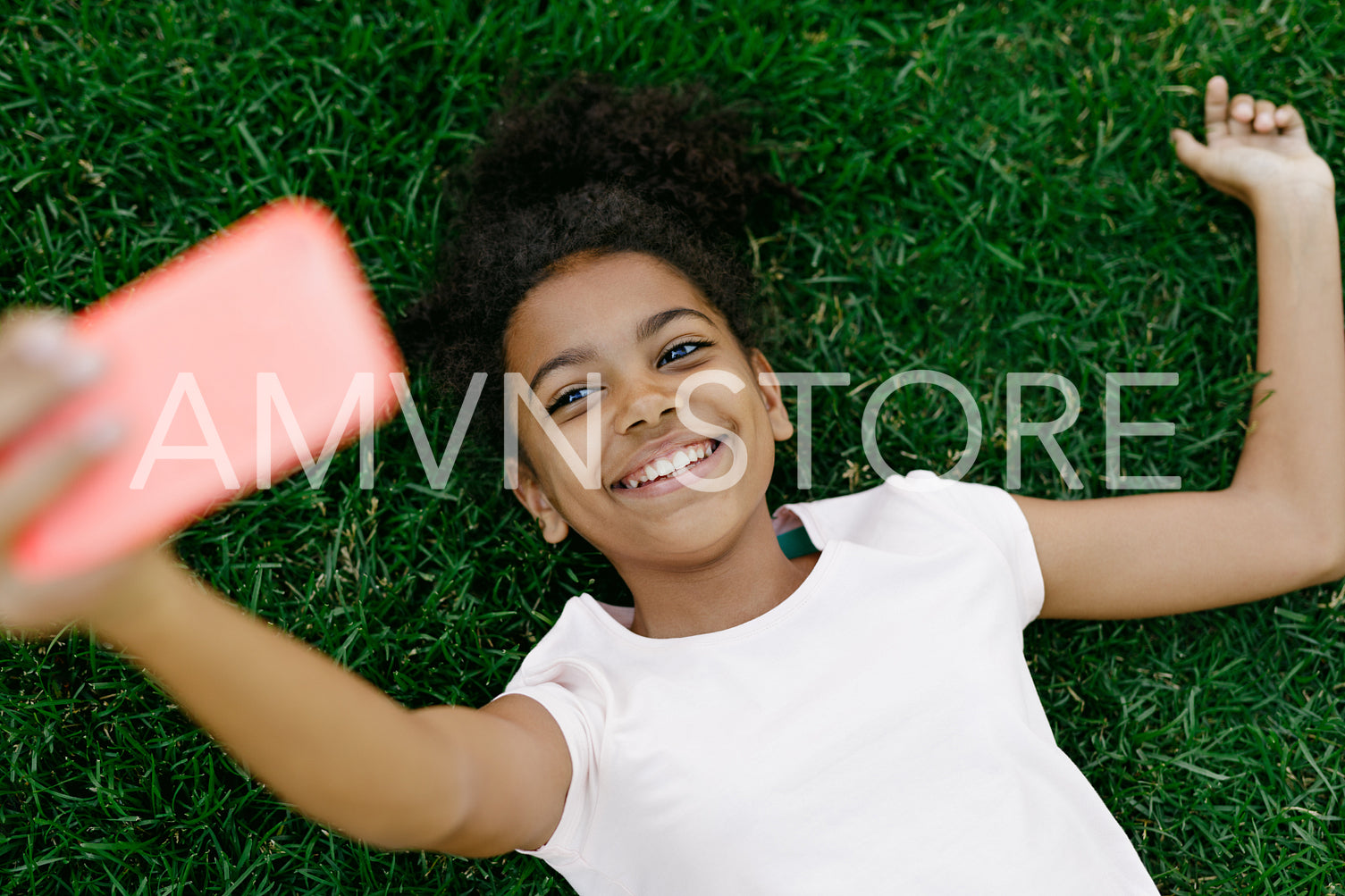 Smiling girl lying on a grass and taking selfie on mobile phone	