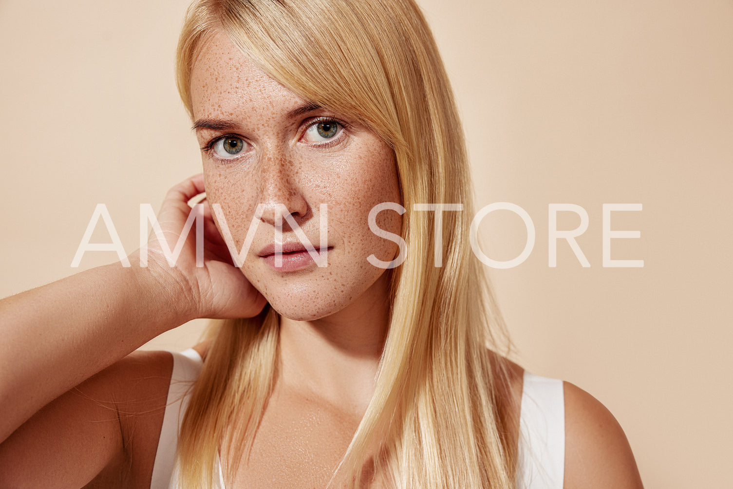 Young beautiful blond woman with freckles looking at the camera and adjusting her hair