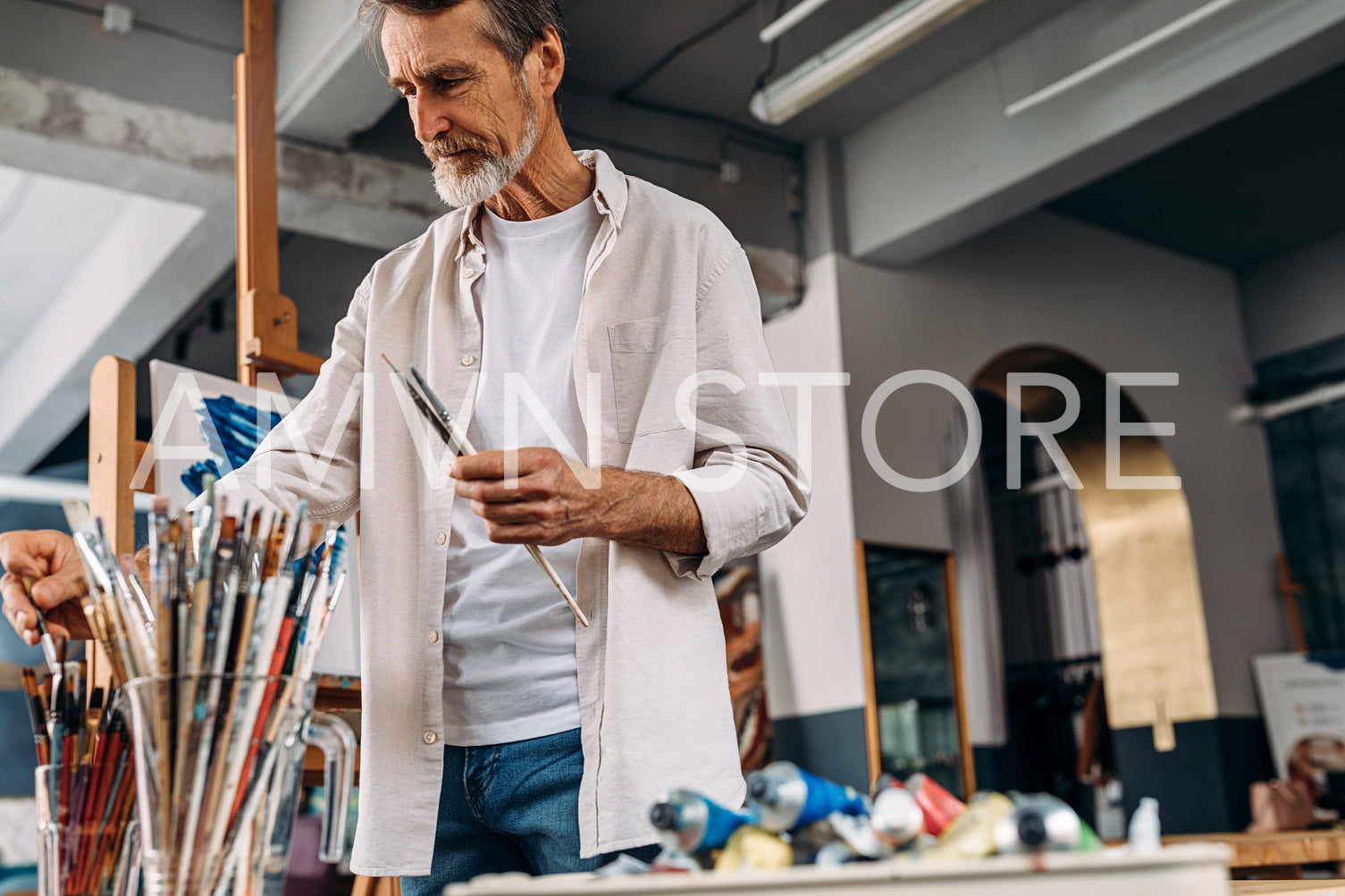 Senior artist standing in studio picking paintbrush for drawing	