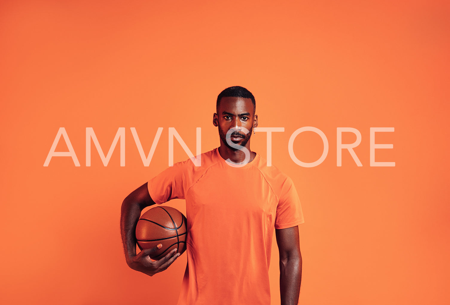 Portrait of a confident young man holding a basket ball against an orange background