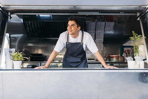 Young salesman standing inside a food truck and looking away while waiting for customers