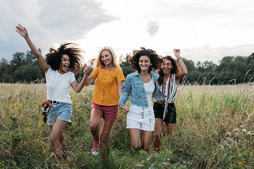 Four laughing women enjoying summer vacation. Happy friends running on the field.