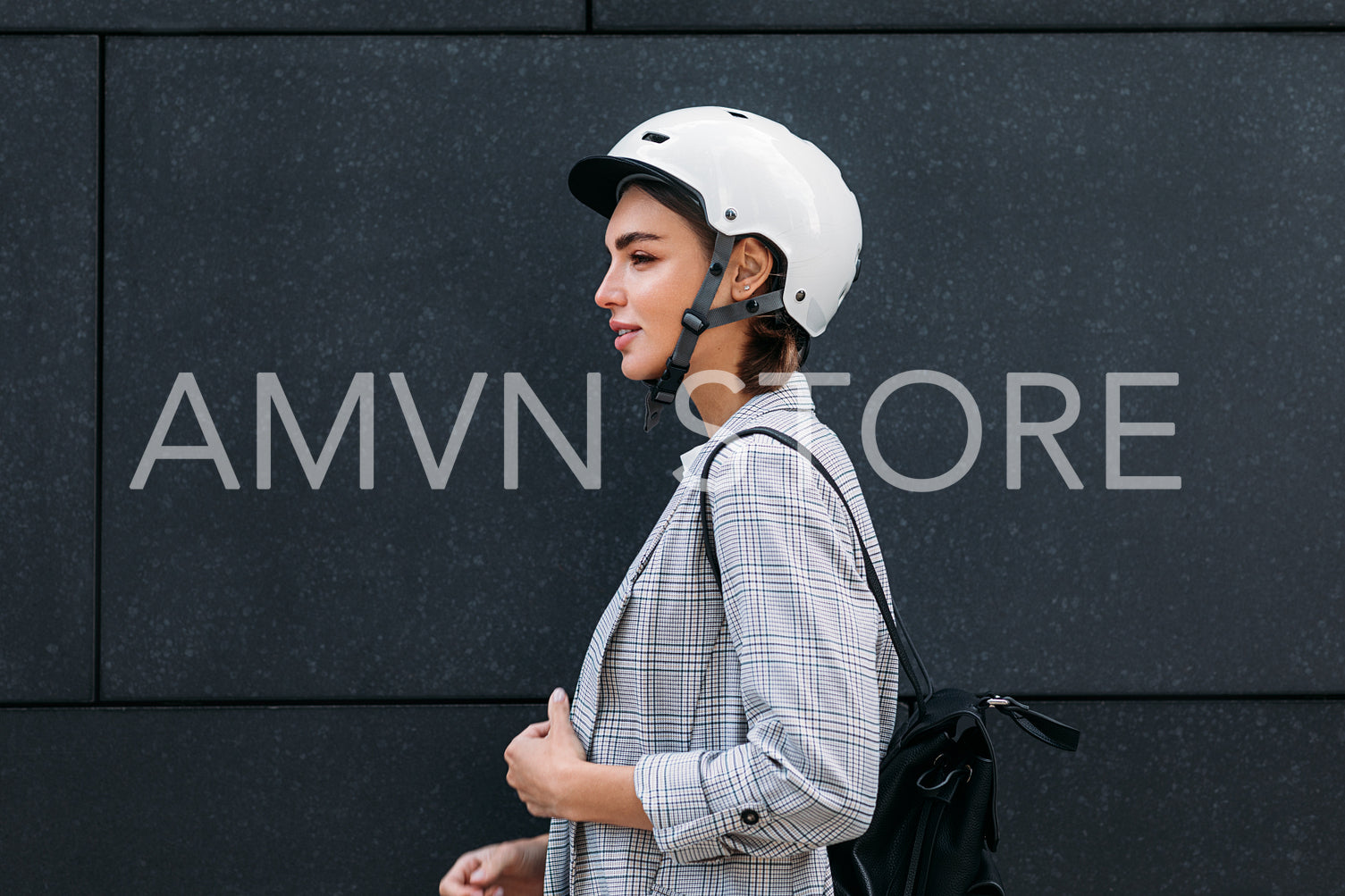 Side view of a good looking businesswoman in cycling helmet standing at black wall in the city