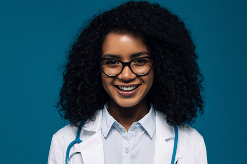 Close up of a beautiful smiling doctor in glasses looking at camera over blue background