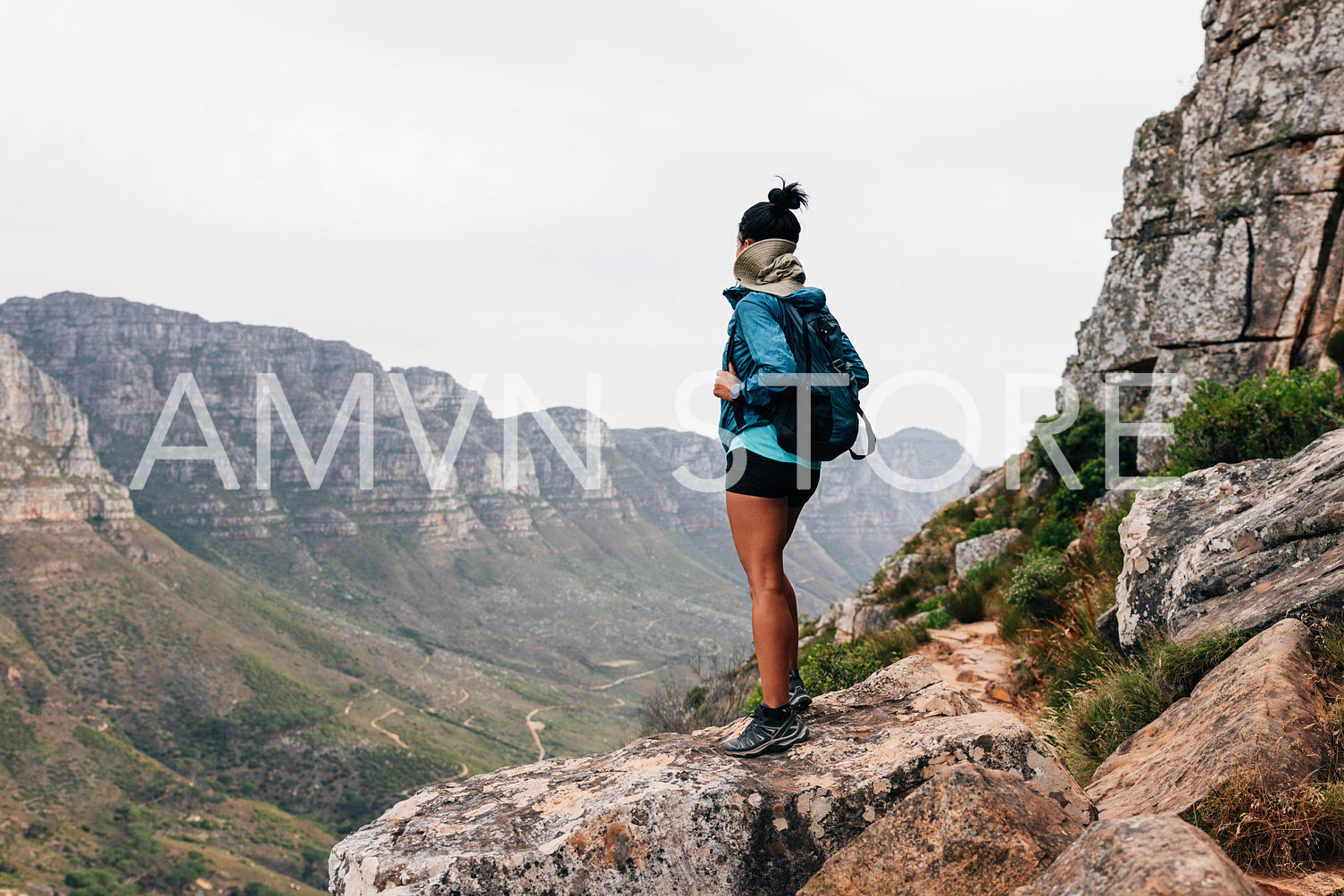 Rear view of a woman with a backpack on a hike. Young female standing on a path enjoying the scenic view from the top.