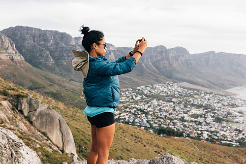 Side view of a woman in sports clothes taking photographs on mobile phone during hiking