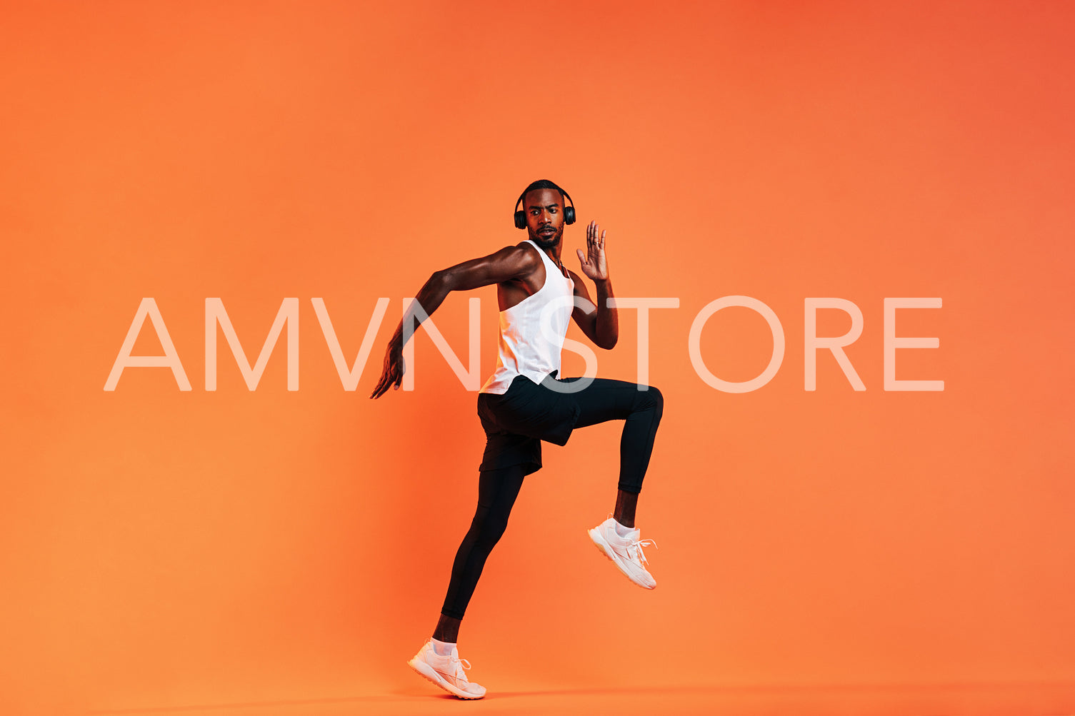 Young athlete in wireless headphones doing intense workout in studio over orange background