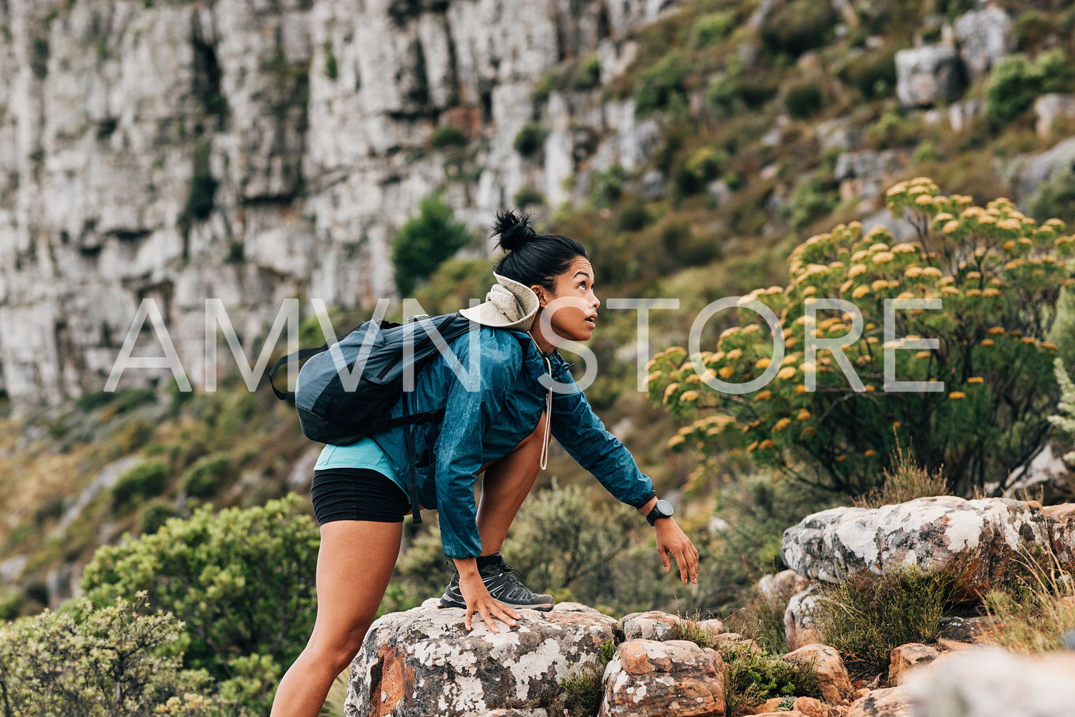 Side view of a woman in sports clothes looking up while climbing up on a rock