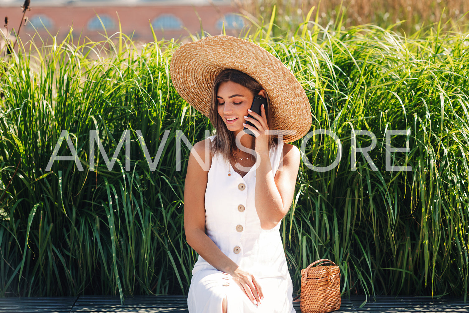 Young beautiful woman talking on a mobile phone while sitting in a park in front of a grass	