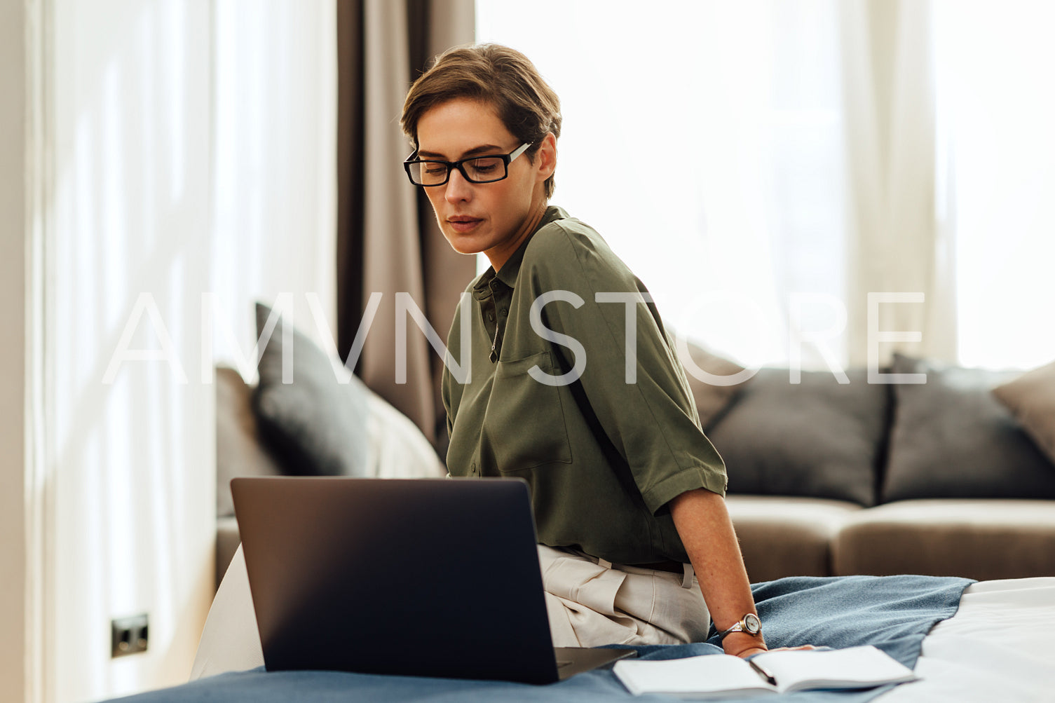 Caucasian woman in casual clothes sitting on bed in hotel room using laptop. Businesswoman working from a modern apartment.	