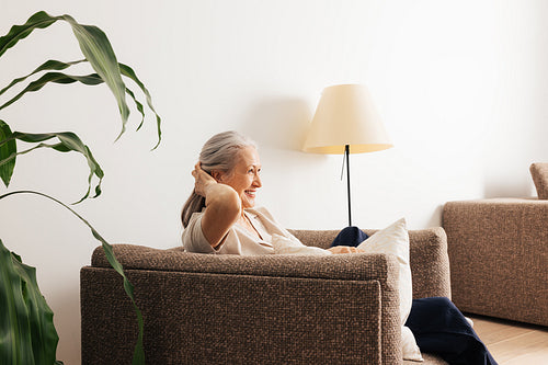 Side view of an aged woman sitting on an armchair in living room