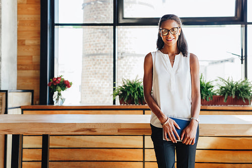 Portrait of successful young entrepreneur leaning to table in cafe