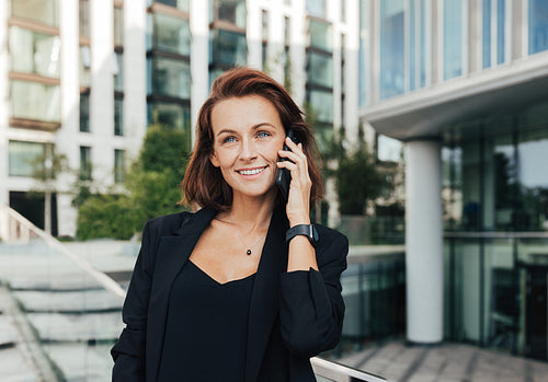 Portrait of a smiling middle-aged female in formal wear making a phone call while standing outdoors