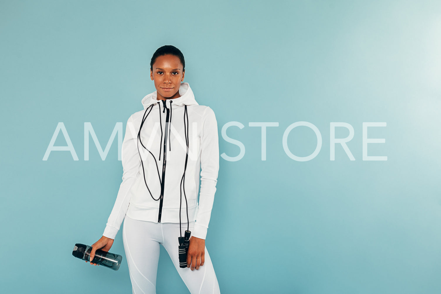 Female fitness model with skipping rope and bottle of a water standing over blue background